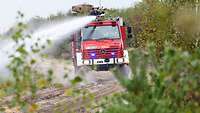Ein Unimog der Bundeswehr-Feuerwehr im Gelände, ein Feuerwehrmann bedient die Löschkanone.
