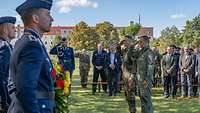 Soldaten salutieren vor einem Gedenkkranz aus Blumen.