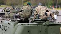 Ein deutscher und ein ukrainischer Soldat sitzen auf einem Panzer und unterhalten sich
