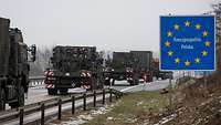 Militärfahrzeuge fahren auf der Autobahn an einem polnischen Grenzübergangsschild vorbei