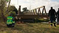 Ein THW-Techniker hockt vor einer Metallbrücke und kontrolliert den Vorschub auf Lagerrollen.