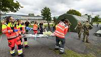 Viele Sanitäter mit Verletzten auf Tragen stehen vor einem grünen Bundeswehrzelt