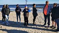 Menschen stehen am Sandstrand und feiern eine Andacht am Meer.