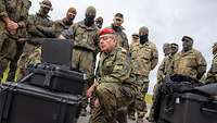 Im Freien schaut ein General auf einen Bildschirm. Im Hintergrund stehen Soldaten im Halbkreis.
