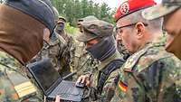 Im Freien schaut ein General auf einen Bildschirm. Im Hintergrund stehen mehrere Soldaten