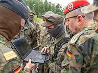 Im Freien schaut ein General auf einen Bildschirm. Im Hintergrund stehen mehrere Soldaten