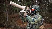 Ein Soldat von der Seite zielt mit einem Jammer in die Luft. Im Hintergrund ein dichter Wald.