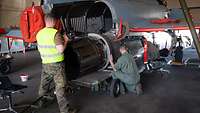 Zwei Bundeswehr-Techniker reparieren in einer Halle das Triebwerk eines Düsenjets