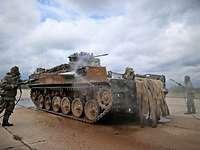 Soldiers in protective suits are cleaning an armored personnel carrier.