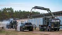Soldiers are decontaminating military vehicles in front of a hall, partly from above using a crane.