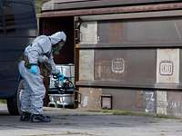 A person in a protective suit holds a device against a railway carriage