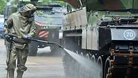  A soldier in NBC protective gear sprays a liquid onto a battle tank.