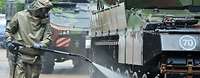  A soldier in NBC protective gear sprays a liquid onto a battle tank.