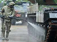 A soldier in NBC protective gear sprays a liquid onto a battle tank.
