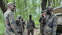 Ein Soldat und Teilnehmende stehen mit Tarnschminke im Gesicht im Halbkreis im Wald zusammen.