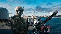 Ein Soldat steht an einer Waffe auf dem Deck eines Kriegsschiffes vor der Skyline Kopenhagens.