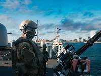 Ein Soldat steht an einer Waffe auf dem Deck eines Kriegsschiffes vor der Skyline Kopenhagens.