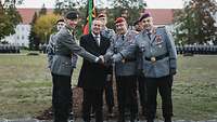 Drei Generale und ein Minister im dunklen Anzug reichen je eine Hand zur Mitte.