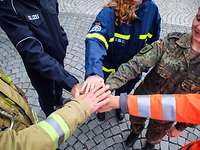 People in different uniforms place their hands on top of each other in a circle