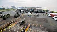  A port. In the foreground a loading ramp, in the background many military vehicles.