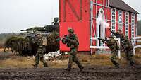  Several soldiers run past a house with their weapons drawn.