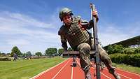  A female soldier in uniform overcomes an obstacle on a sports track.