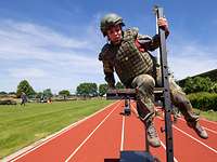  A female soldier in uniform overcomes an obstacle on a sports track.