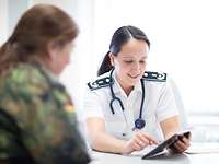 A woman sits behind a table and explains something on a tablet.