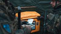  Two soldiers throw postcards into a field post office mailbox.