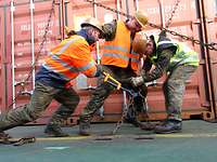 Three soldiers secure a container on the deck of a ship.