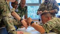 Soldaten unterschiedlicher Nationen stehen an einem Tisch und bauen etwas