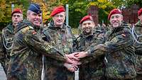 Vier Soldaten halten sich die Hände und blicken in die Kamera.