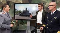 „Nachgefragt“ mit Flottillenadmiral Christian Bock und Ministerialdirigent Alexander Schott Zwei Soldaten und ein Mann stehen an einem Tisch vor einem Monitor und sprechen miteinander