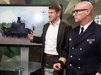 Zwei Soldaten und ein Mann stehen an einem Tisch vor einem Monitor und sprechen miteinander