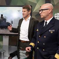 Zwei Soldaten und ein Mann stehen an einem Tisch vor einem Monitor und sprechen miteinander