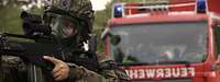 Ein Soldat mit Gasmaske und Gewehr vor einem Feuerwehrauto
