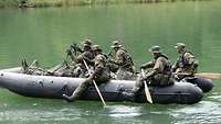Fünf Soldaten sitzen in einem schwarzen Schlauchboot und paddeln über ein Gewässer.