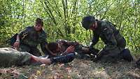 Zwei offenbar verletzte Soldaten liegen auf dem Waldboden, zwei weitere kümmern sich um sie.