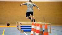 Eine Person springt in einer Sporthalle über mehrere Hindernisse.