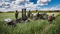 Soldaten stehen neben mehreren Kisten und einem Gabelstapler im Feld 