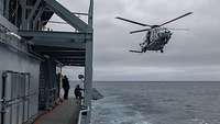 Ein Hubschrauber fliegt neben einem fahrenden Schiff über ein Gewässer