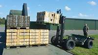Ein Soldat bedient mit der Fernsteuerung einen Gabelstapler, der Munitionspaletten auf einen LKW hebt