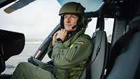 Ein Pilot sitzt im Cockpit eines Hubschraubers und legt seinen Helm an