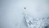 Ein Hubschrauber fliegt im verschneiten Gebirge mit Wolken