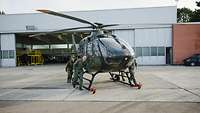 Soldaten und Zivilisten schieben einen Hubschrauber aus dem Hangar