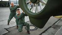 Zwei Männer im Overall der Bundeswehr schieben einen Hubschrauber aus einer Halle heraus.