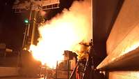 Auf einem Schiff der Marine ist der Feuerball einer startenden Rakete zu sehen.