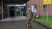 Ein Soldat mit goldgelber Kordel an der rechten Schulter steht vor einem roten Backsteingebäude