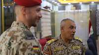 Ein deutscher Soldat steht in Uniform mit rotem Barett neben einem irakischen General.