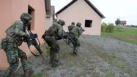 Zwei niederländische und zwei deutsche Soldaten laufen mit den Waffen im Anschlag auf ein Haus zu.